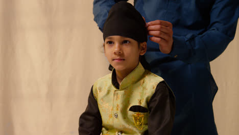 Studio-Shot-Of-Father-Tying-Turban-Onto-Head-Of-Young-Sikh-Son-Wearing-Traditional-Waistcoat-As-Sequence-Part-4-Of-10